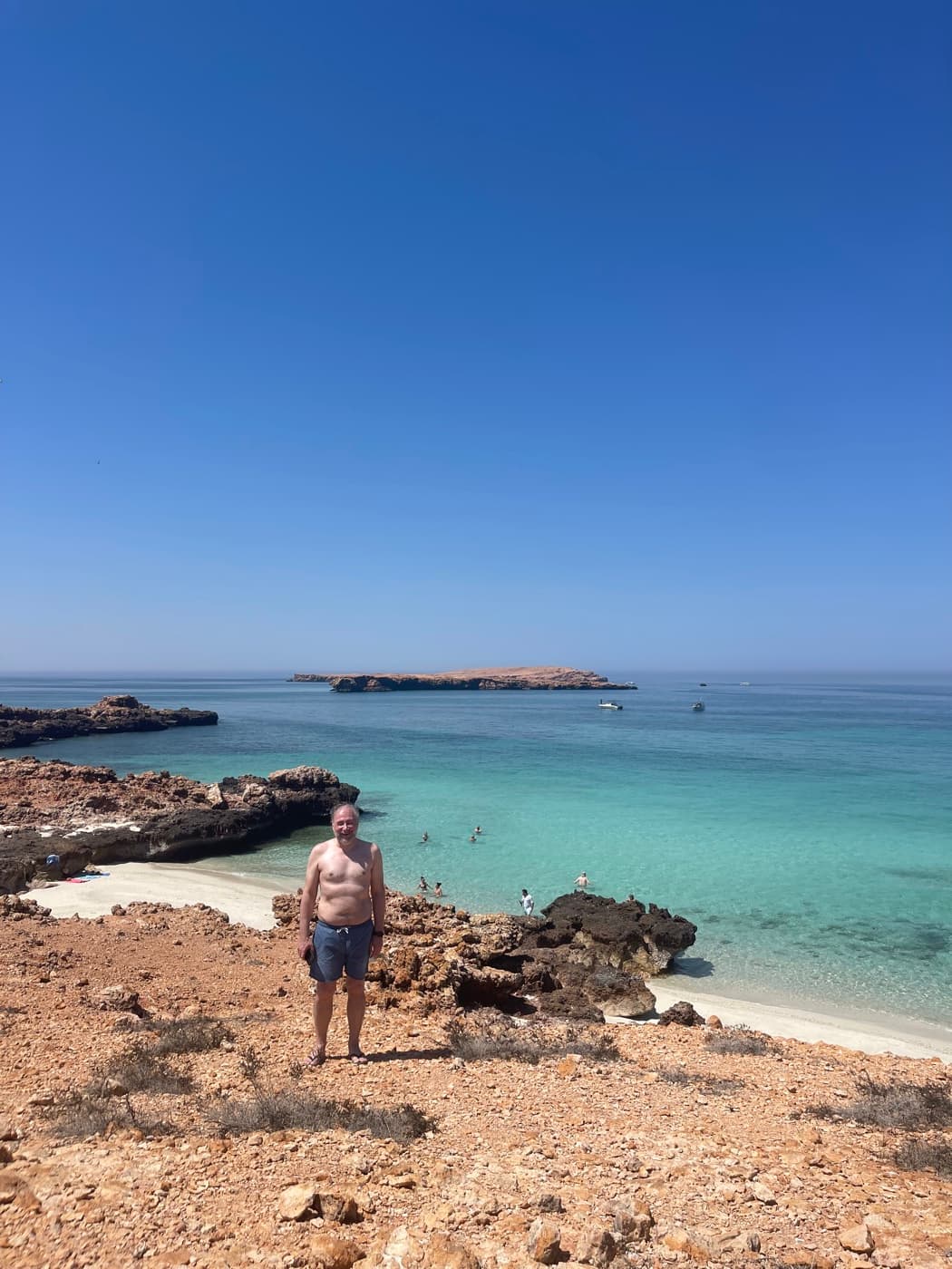 A visitor on the rocky shore of a Daymaniyat island with turquoise sea behind, near Muscat