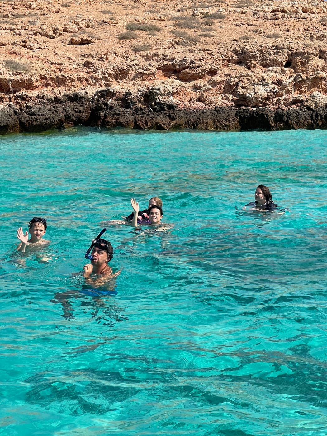 Snorkellers in clear turquoise water beside a Daymaniyat island on a half-day tour from Muscat